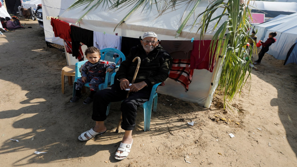 رجل فلسطيني نازح أبو وائل نصر الله يجلس بجوار حفيده بالقرب من خيمتهم حيث يحتمون، في مستشفى ناصر في خان يونس، جنوبي قطاع غزة، 2 ديسمبر 2023. (رويترز)