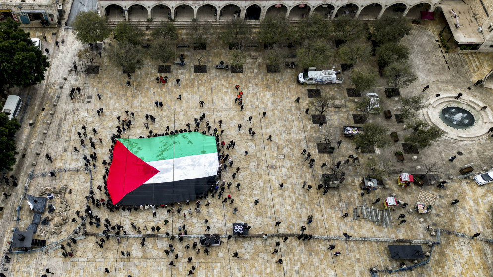 رفع العلم الفلسطيني في أثناء تجمع خارج كنيسة المهد في مدينة بيت لحم في الضفة الغربية المحتلة. (أ ف ب)