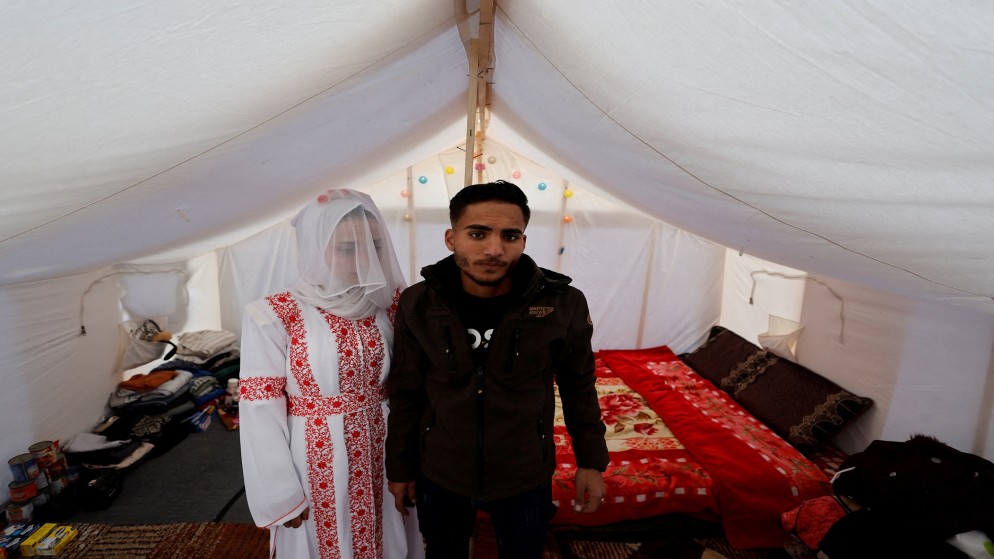 زوجان فلسطينيان، محمد الغندور وعروسه شهد، يقفان في مخيم، وسط العدوان الإسرائيلي المستمر على قطاع غزة في يوم زفافهما، في رفح بجنوب قطاع غزة، 18 يناير 2024. (رويترز)