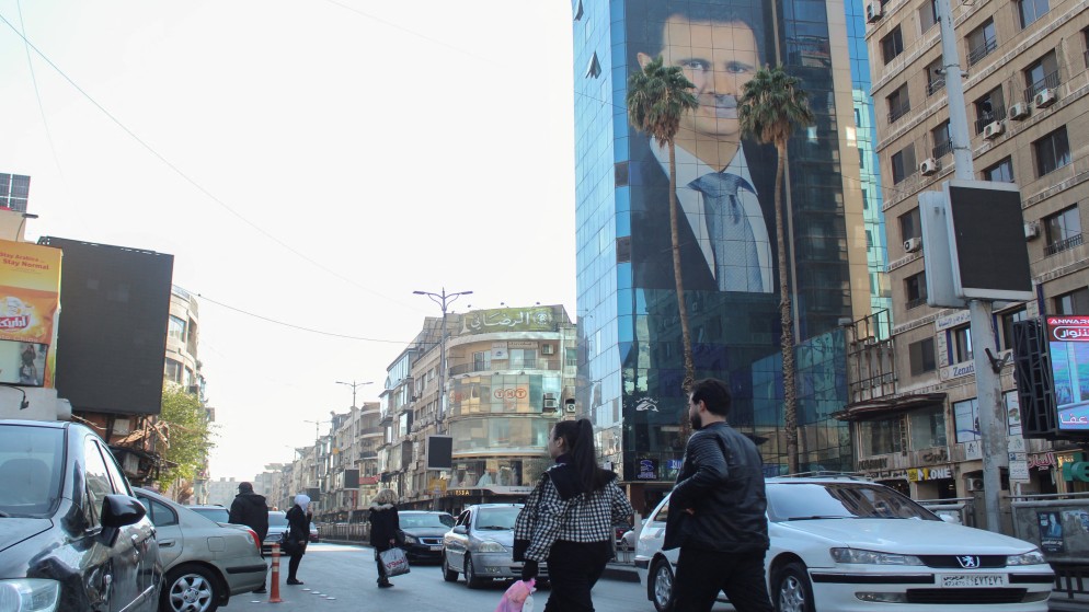 أشخاص يسيرون بالقرب من ملصق الرئيس السوري بشار الأسد في دمشق، بعد استيلاء المعارضة على حلب. 5 ديسمبر 2024.