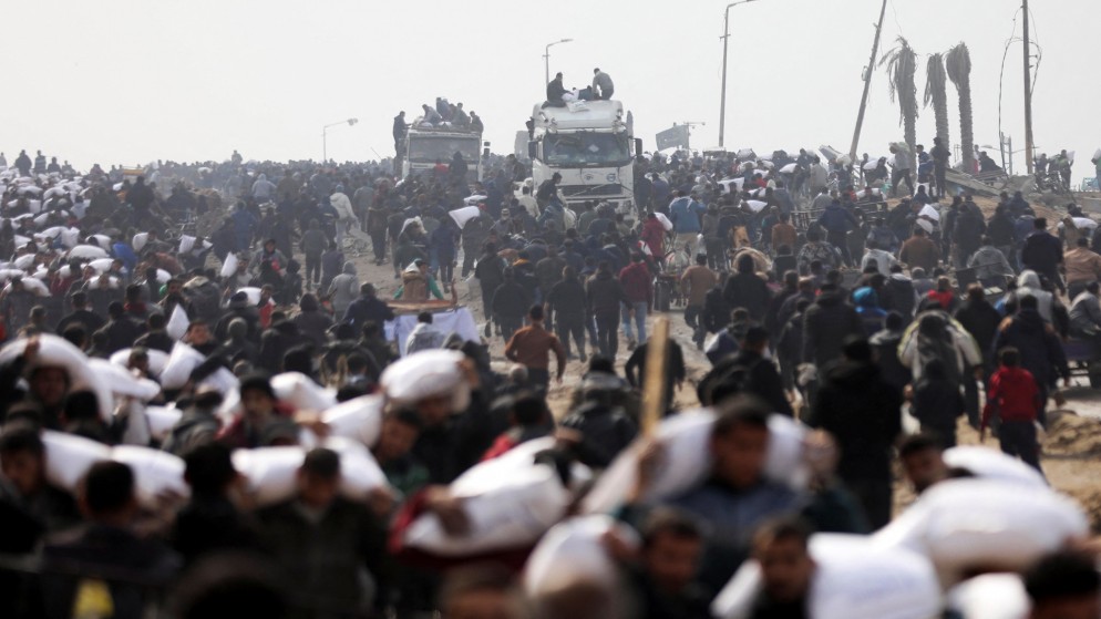 فلسطينيون يحملون أكياس الطحين التي حصلوا عليها من شاحنة مساعدات بالقرب من نقطة تفتيش إسرائيلية في مدينة غزة، 19 شباط/ فبراير 2024. (رويترز)