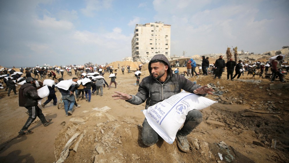 فلسطينيون يحملون أكياس الدقيق التي حصلوا عليها من شاحنة مساعدات بالقرب من نقطة تفتيش إسرائيلية، في مدينة غزة، 19 شباط/فبراير 2024. (رويترز)