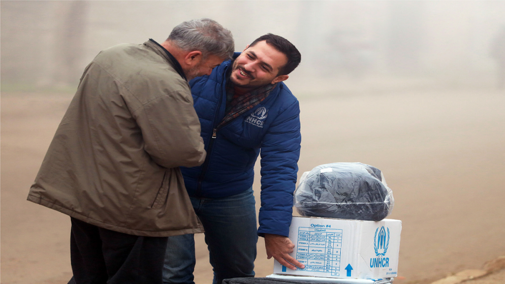 صورة أرشيفية لموظف في المفوضية السامية للأمم المتحدة لشؤون اللاجئين يوزع مواد إغاثة أساسية لفصل الشتاء على عائلة نازحة في محافظة حمص في سوريا. (UNHCR)