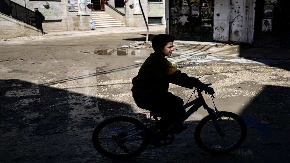 صبي فلسطيني يركب دراجة على طريق موحل في مخيم جنين للاجئين في الضفة الغربية المحتلة.  20 مارس 2024 ت(أ ف ب)