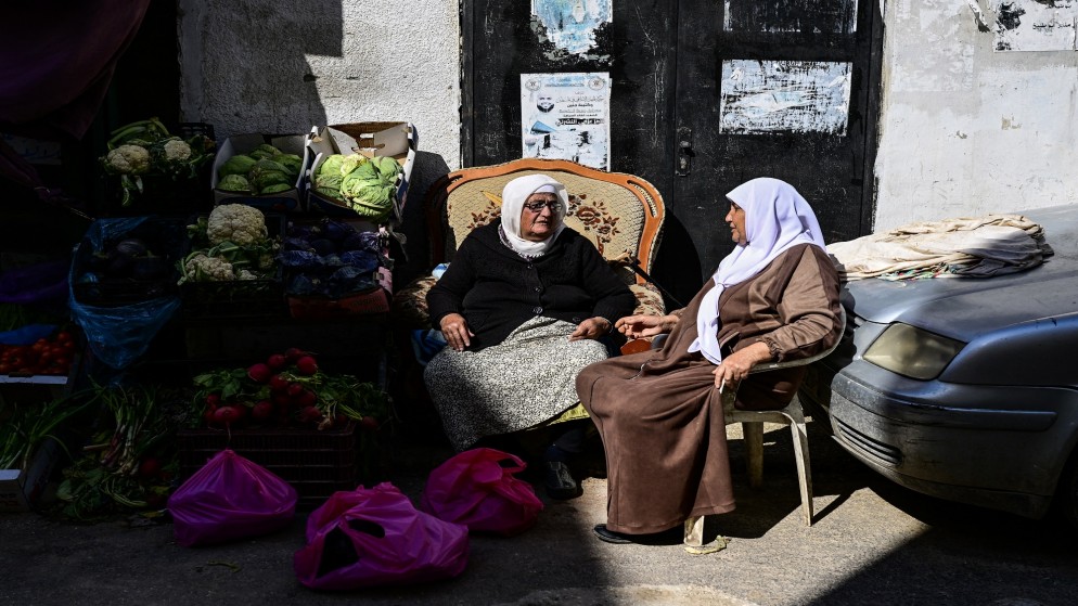 امرأة فلسطينية تبيع الخضروات في كشك في الشارع وهي تتحدث مع سيدة خلال شهر رمضان المبارك في مخيم جنين للاجئين في الضفة الغربية المحتلة. 20 مارس 2024،.(أ ف ب)
