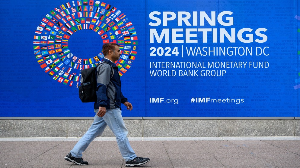 شاب يسير بجانب لافتة اجتماعات الربيع 2024 لصندوق النقد والبنك الدوليين في واشنطن. (أ ف ب)