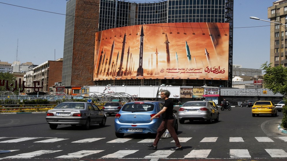 رجل يعبر الشارع بينما يمر سائقو السيارات أمام لوحة إعلانية تصور الصواريخ البالستية الإيرانية في طهران .19 نيسان 2024. (أ ف ب)