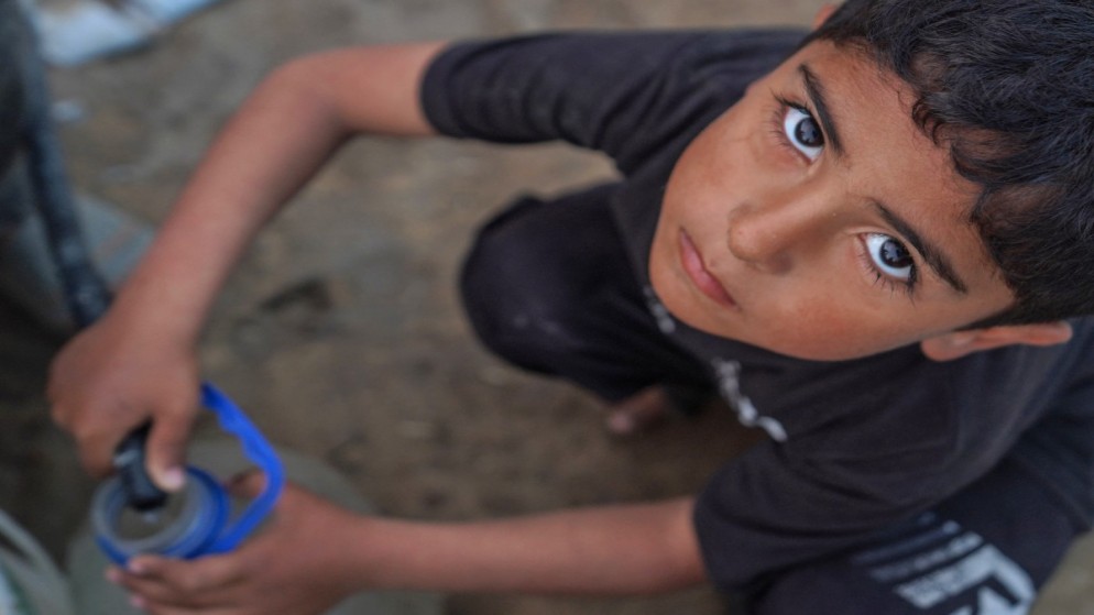 صبي فلسطيني يملأ قارورة ماء من خرطوم في دير البلح بوسط قطاع غزة، 19 نيسان 2024. (أ ف ب)
