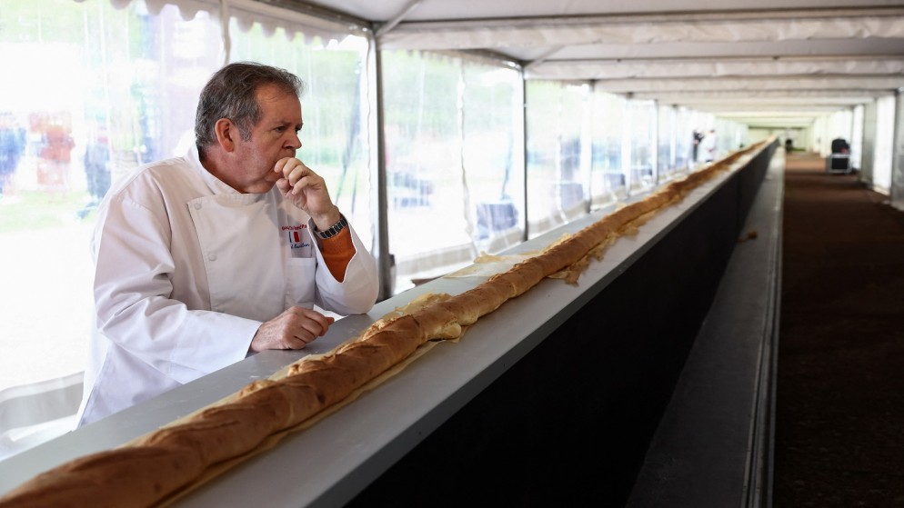 خباز فرنسي يقف بالقرب من أطول رغيف خبز فرنسي في العالم خلال معرض سورينس للخبز الفرنسي في سورينس بالقرب من باريس، فرنسا، 5 أيار 2024. (رويترز)