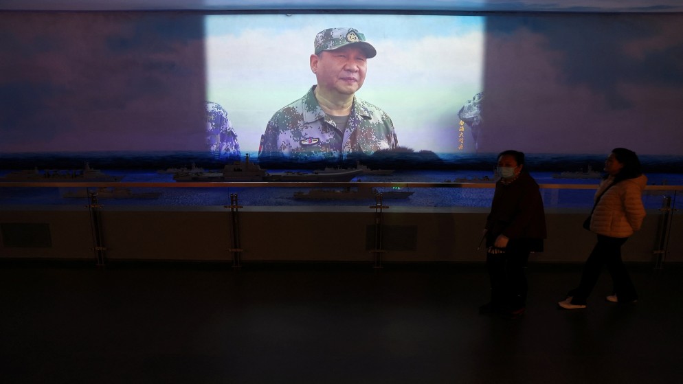 زوار يمرون بجوار عرض فيديو يحتوي على لقطات للرئيس الصيني شي جين بينغ وهو يتفقد عرضًا بحريًا في بحر الصين الجنوبي. 23 أبريل 2024. (رويترز)