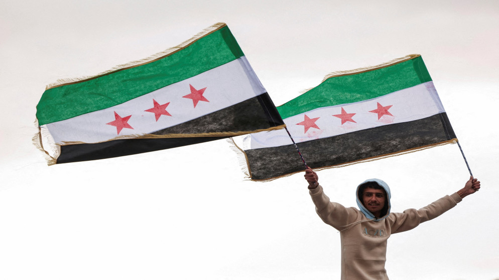 شخص يحمل رايات العلم السوري في دمشق. سوريا، 27 كانون الأوّل 2024. (رويترز)