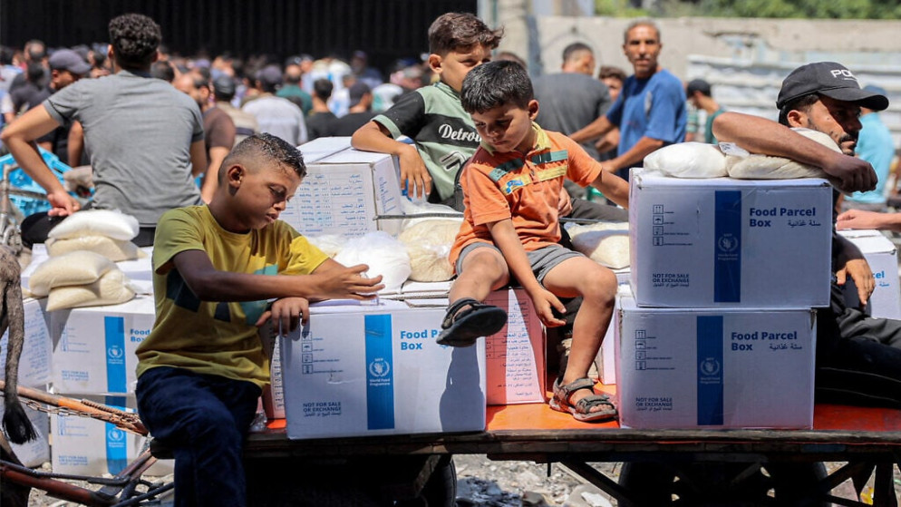 أطفال فلسطينيون يجلسون على عربة محملة بطرود مساعدات مقدمة من (الأونروا) في وسط مدينة غزة. 27 آب 2024. (أ ف ب)