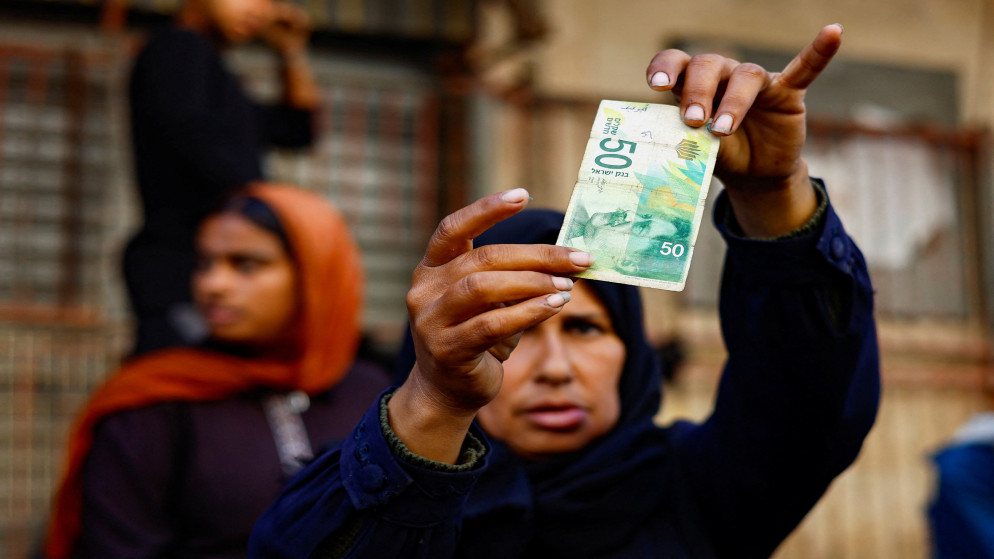 منال الصعيدي، فلسطينية تفحص ورقة نقدية تالفة أثناء إصلاحها نقودًا في أحد شوارع النصيرات، وسط غزة، 27 تشرين الأول  2025. (رويترز)