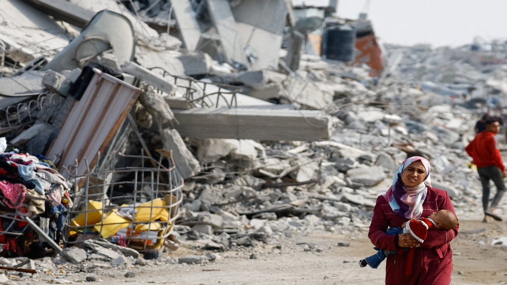 امرأة فلسطينية تحمل طفلاً رضيعًا تسير بين أنقاض المباني المدمرة، وسط وقف إطلاق النار بين إسرائيل وحماس، في مدينة غزة، 2 تشرين الثاني 2025. )رويترز(