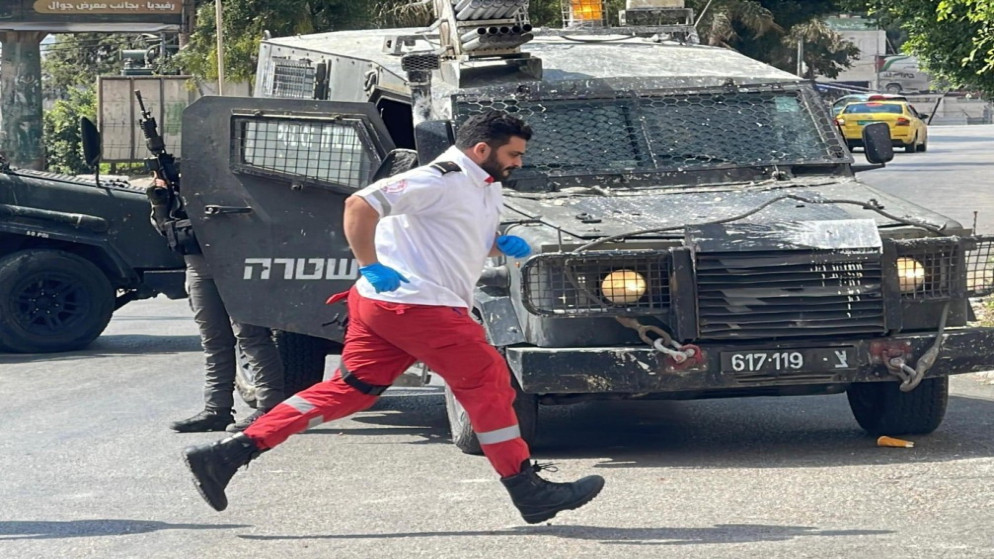 أحد طواقم الهلال الأحمر الفلسطيني أمام مركبة عسكرية تابعة لجيش الاحتلال الإسرائيلي.