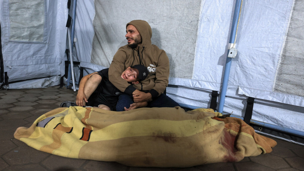 رجل وطفل فلسطيني أمام جثمان شهيد في مستشفى الأهلي العربي في مدينة غزة 19 تشرين الثاني 2025. (رويترز)