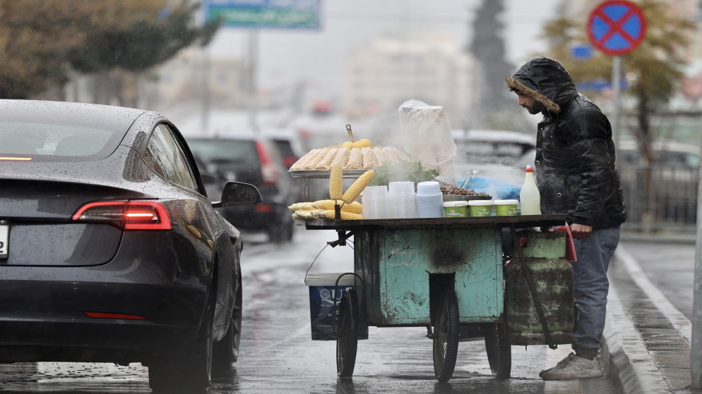 بائع متجول في شارع رئيسي في عمّان خلال أجواء ماطرة. (المملكة)