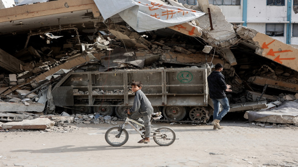 طفل يتجوّل على دراجة هوائية وبجواره دبابة إسرائيلية هدم عليها منزل في غزة. (أ ف ب)