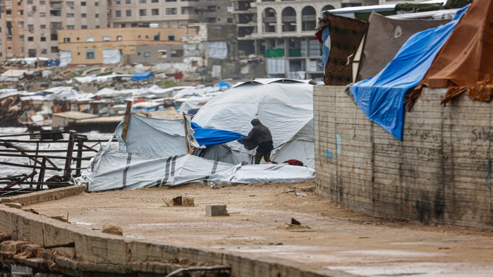 رجل فلسطيني نازح يقوم بتعديل قماش خيمة عائلته التي أقيمت في الميناء، في ظل هطول الأمطار وبرودة الشتاء التي تشهدها المنطقة، في مدينة غزة .28 ديسمبر 2025.(أ ف ب)