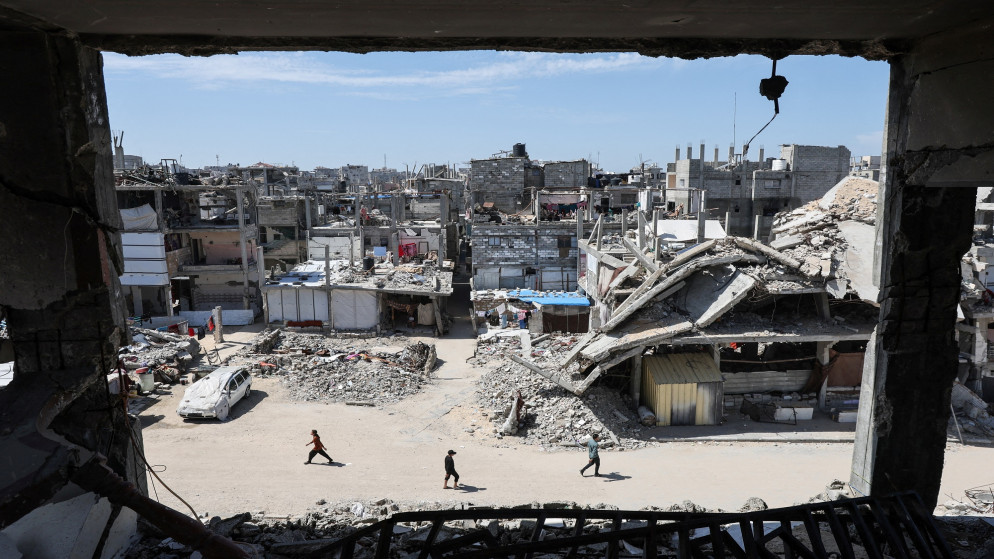 فلسطينيون يسيرون بالقرب من أنقاض منازل في خان يونس جنوبي قطاع غزة. 27 آذار 2025. (رويترز)