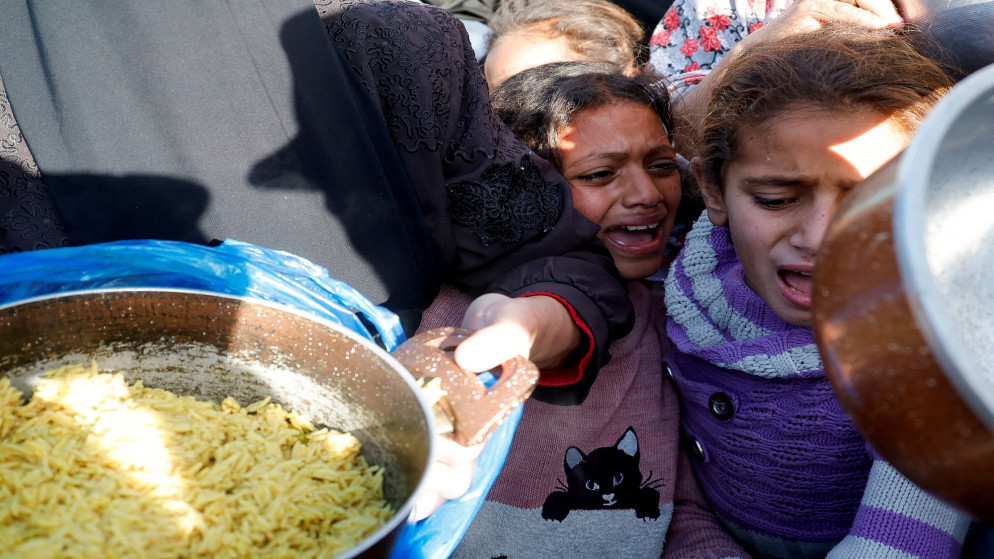 أطفال فلسطينيون يبكون أثناء انتظارهم لتلقي الطعام الذي أعده مطبخ خيري، في رفح، جنوب قطاع غزة، 13 آذار 2025. (رويترز)