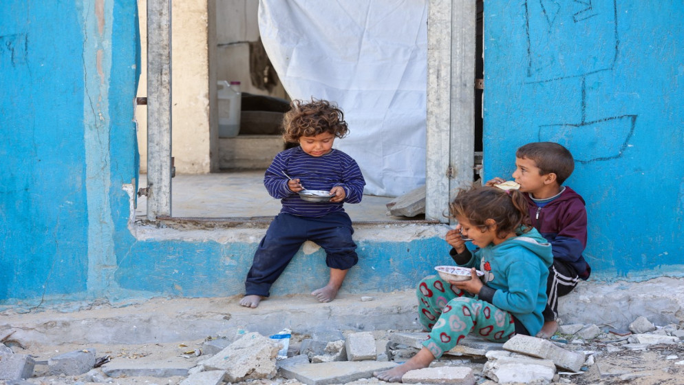أطفال فلسطينيون يتناولون الطعام وهم يجلسون قرب باب منزل متضرر في مدينة غزة. 1 مايو/أيار 2025. (أ ف ب)