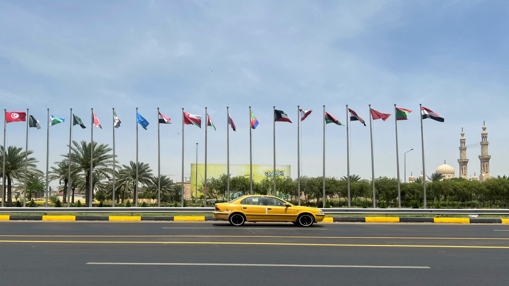 سيارة أجرة تمر أمام أعلام الدول الأعضاء في جامعة الدول العربية المعروضة على طول الشارع قبل انعقاد القمة العربية الرابعة والثلاثين في بغداد، العراق، 15 أيار/ مايو 2025. (رويترز/ أحمد سعد)