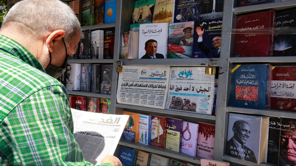 مواطن يقرأ صحيفة محلية بعنوان رئيسي على صفحتها الأولى عن آخر الأحداث أمام كشك في العاصمة عمان. 04/04/2021. (خليل مزرعاوي/ أ ف ب)
