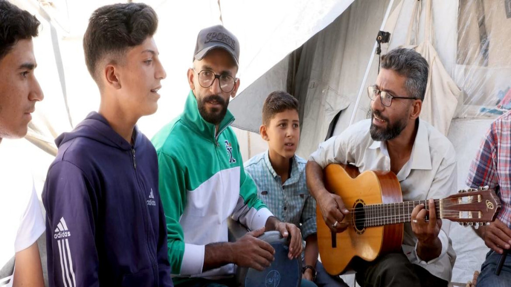 أحمد أبو عمشة محاط بالأطفال لعزف الموسيقى والغناء وتعلم الموسيقى من خيمته في قطاع غزة. (الأمم المتحدة)
