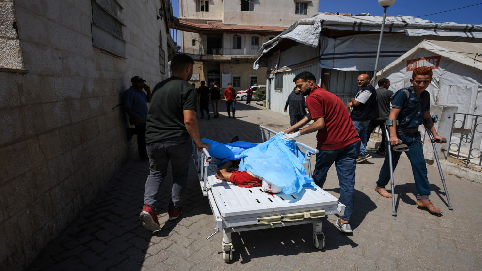 فلسطينيان يقفان إلى جانب جثمان شهيد استشهد في غارة جوية إسرائيلية استهدفت مستشفى الأهلي العربي، 5 حزيران 2025. (رويترز)
