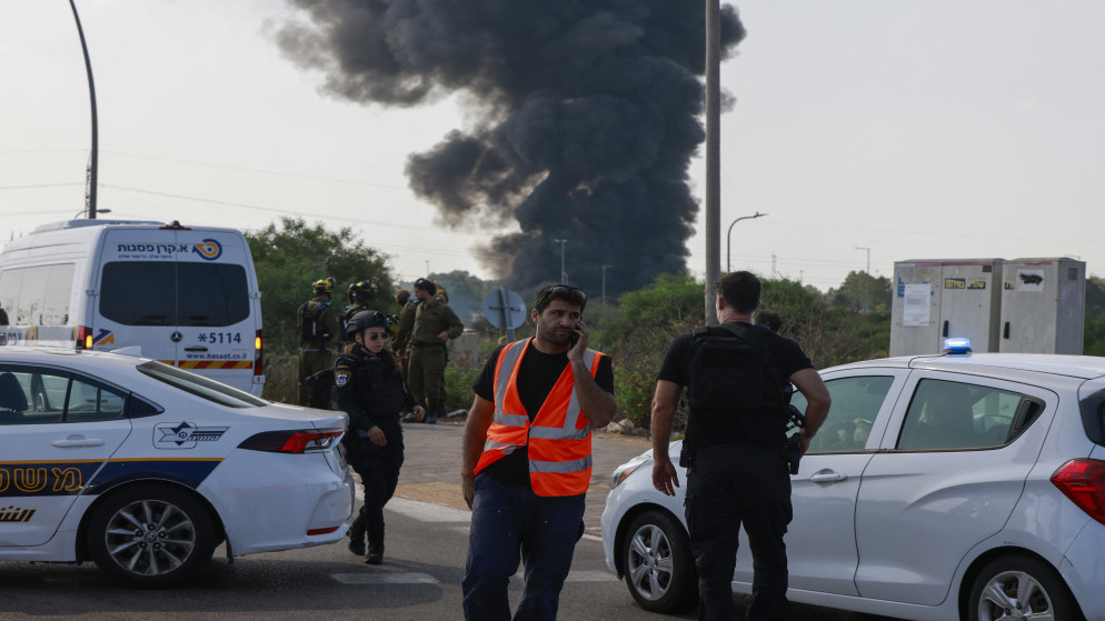 خدمات الطوارئ الإسرائيلية وأفراد الشرطة على طريق مغلق بينما يتصاعد الدخان من موقع في هرتسليا بالقرب من تل أبيب بعد وابل جديد من الصواريخ الإيرانية في 17 حزيران 2025. (أ ف ب)