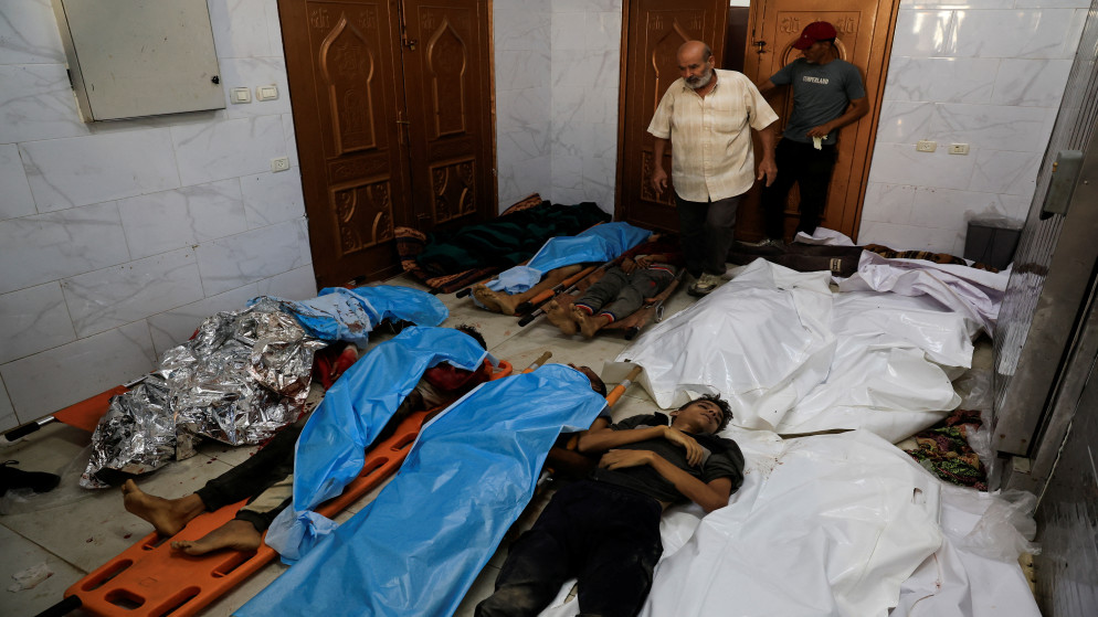 أشخاص يسيرون بجوار جثامين شهداء فلسطينيين في مستشفى ناصر في خان يونس جنوب قطاع غزة، 16 تموز 2025. (رويترز)