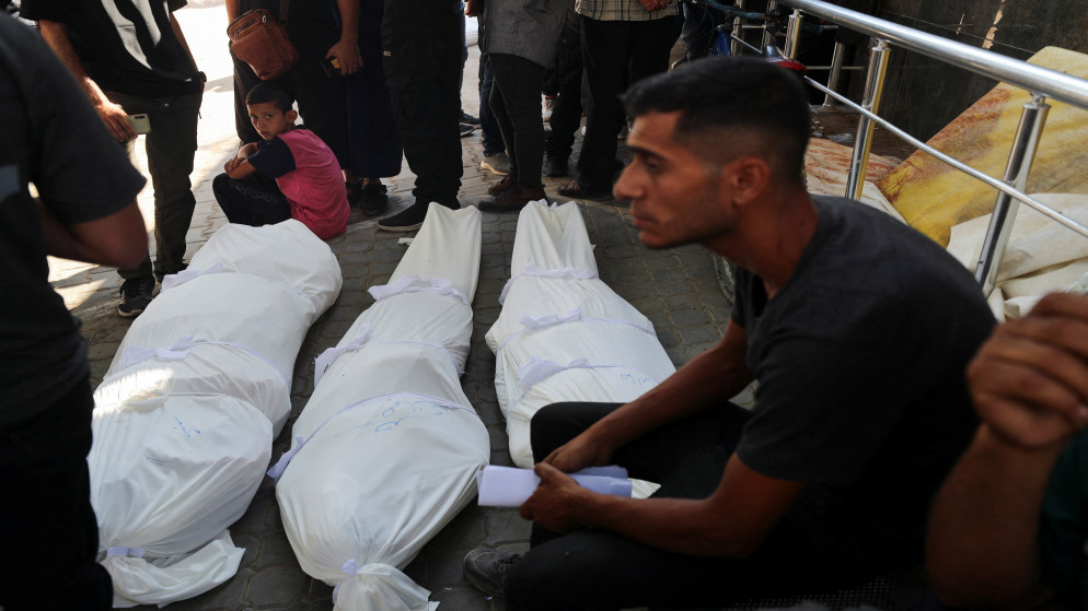 فلسطينيون يجلسون بالقرب من جثامين شهداء في مستشفى الشفاء في مدينة غزة. 13 تموز 2025. (رويترز)