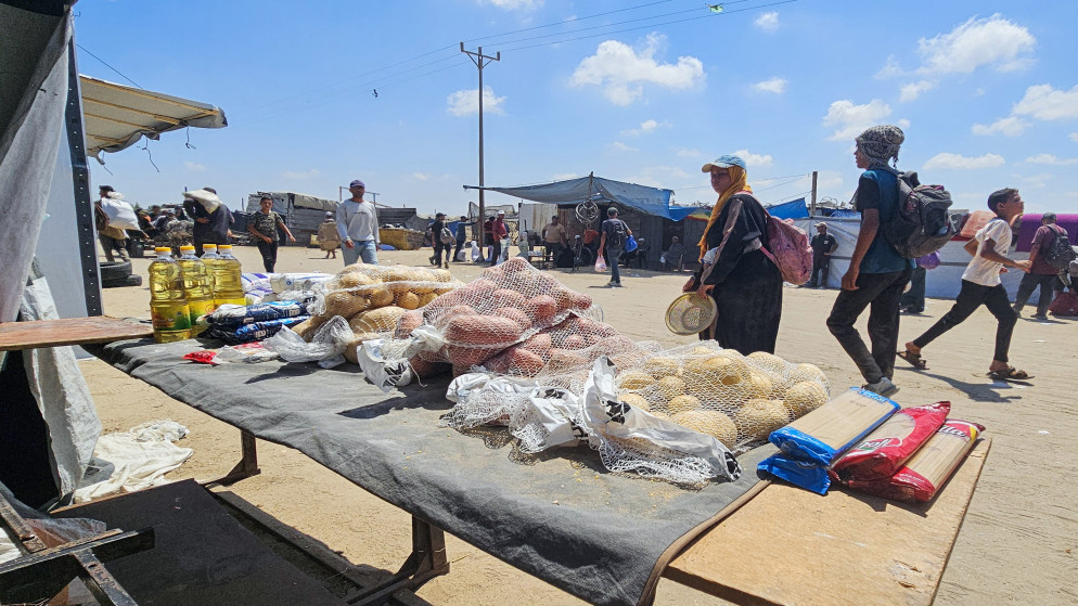 فلسطينيون يستعرضون مواد غذائية معروضة للبيع في سوق مؤقت بمنطقة المواصي برفح، وسط ارتفاع حاد في أسعار المواد الغذائية الشحيحة أصلًا في قطاع غزة المحاصر، 20 تموز 2025. (أ ف ب)