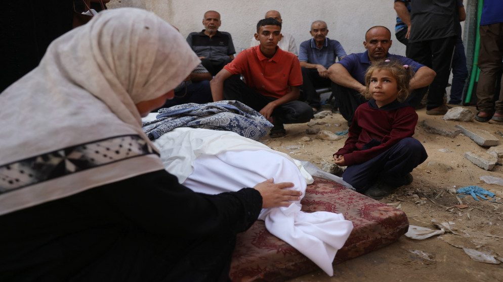 فلسطينيون يجلسون بالقرب من جثمان أحد الشهداء في مدينة غزة، 23 تموو 2025. (أ ف ب)