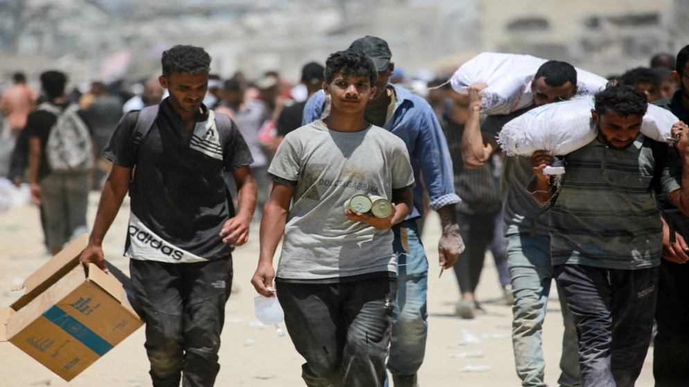 فلسطيني يحمل طعاما معلبا بينما ينقل آخرون كميات من الدقيق حصلوا عليها في جباليا شمال قطاع غزة. 1 آب 2025. (أ ف ب)