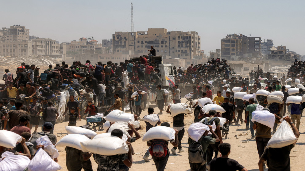 فلسطينيون يحملون أكياس طحين بعد دخول الشاحنات المحملة بالمساعدات الإنسانية إلى شمال غزة في 27 تموز 2025. (أ ف ب)