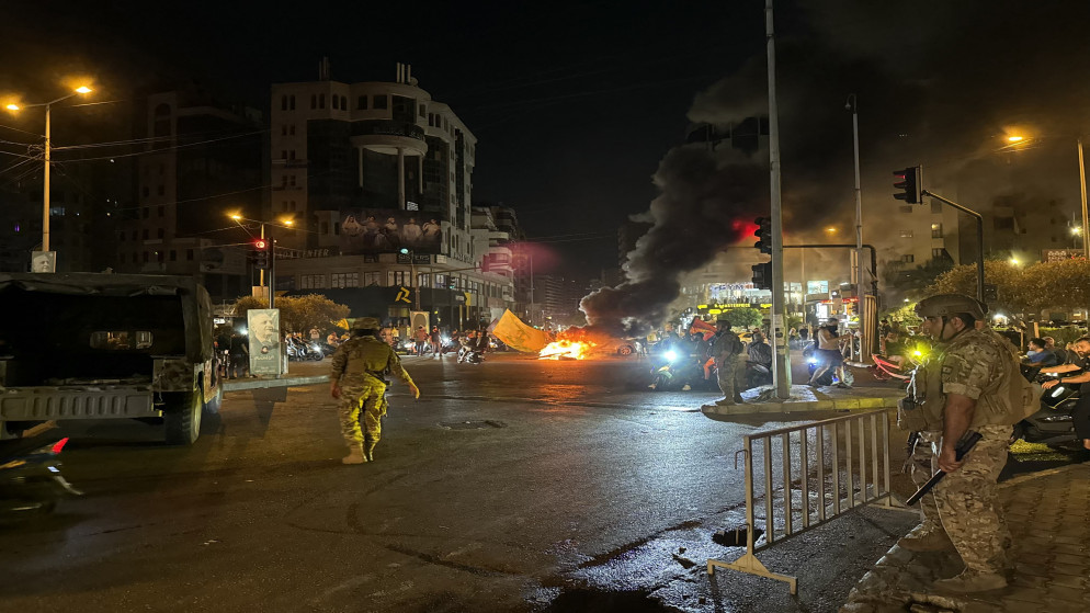 جنود لبنانيون يراقبون أنصار حزب الله وهم يقطعون الشوارع بإطارات مشتعلة، ويتظاهرون بالسيارات والدراجات النارية احتجاجا على موافقة الحكومة على خطة لنزع سلاحه، في الضاحية الجنوبية لبيروت، 8 آب 2025. (أ ف ب)