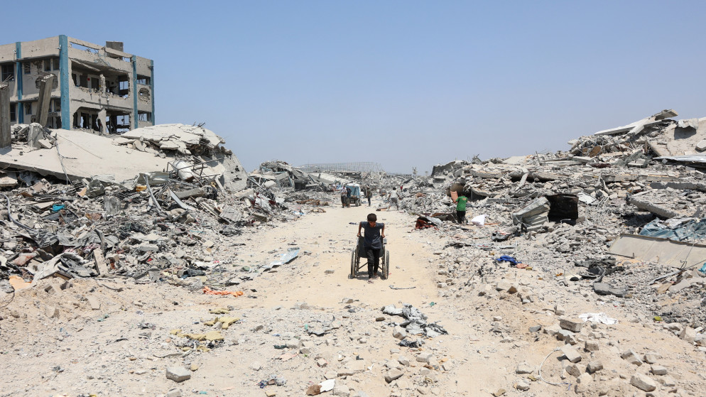 فتى فلسطيني يجر كرسيا متحركا أمام مبان مدمرة في حي التفاح بمدينة غزة، 14 آب 2025. (أ ف ب)