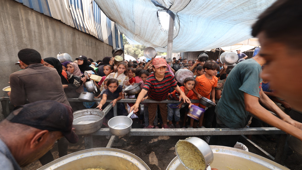 فلسطينيون يتجمعون لاستلام وجبات مطبوخة من مركز توزيع أغذية في مخيم النصيرات للاجئين وسط قطاع غزة، 18 آب 2025. (أ ف ب)