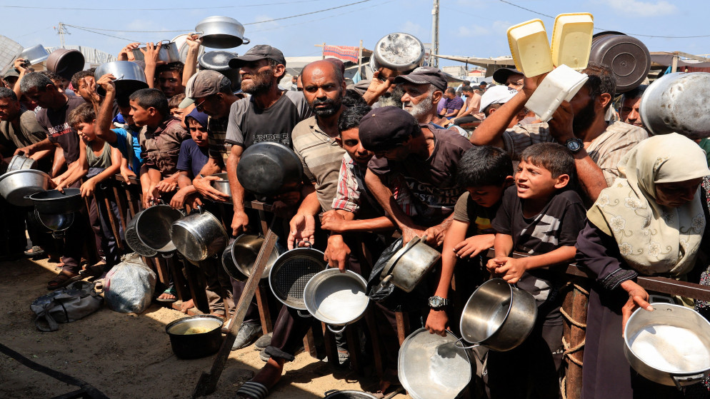فلسطينيون يحملون أوانيَ في انتظار الحصول على الطعام من مطبخ في خان يونس جنوبيّ قطاع غزة. 21 آب 2025. (رويترز)