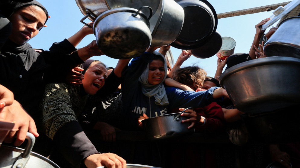 فلسطينيون يحملون أواني في انتظار الحصول على الطعام من مطبخ في خان يونس جنوبي قطاع غزة. 21 آب 2025. (رويترز)