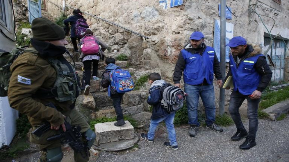 شبان فلسطينيون يصطحبون أطفالًا إلى المدارس في مدينة الخليل بالضفة الغربية.