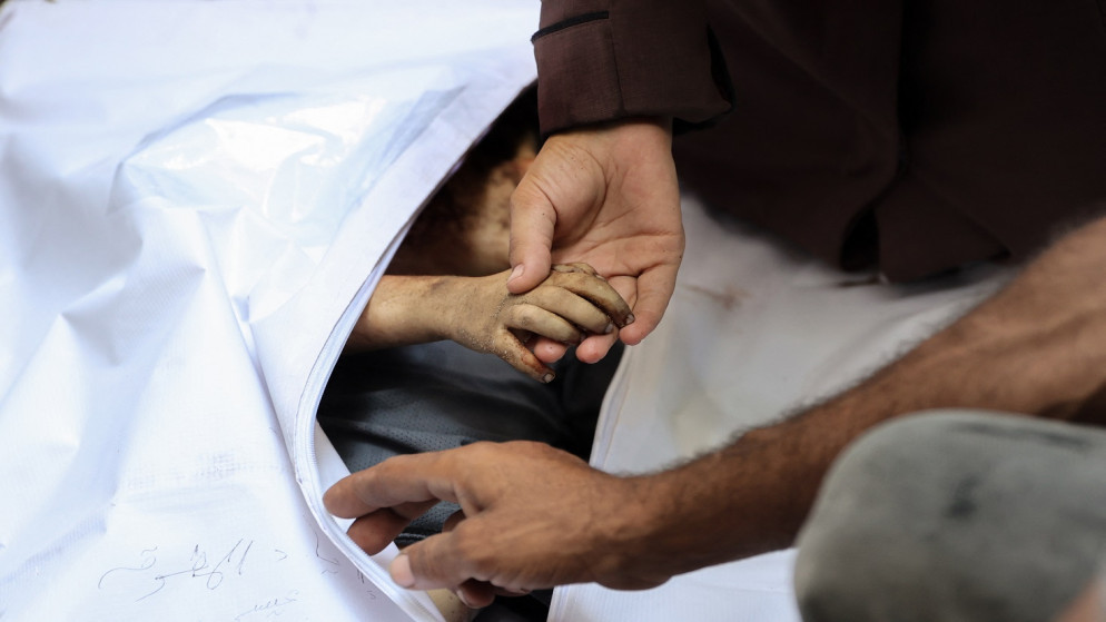 امرأة فلسطينية تمسك بيد طفل قُتل في غارة إسرائيلية على مخبز مؤقت في خيمة بشارع النصر بمدينة غزة، في 30 آب 2025. (أ ف ب)