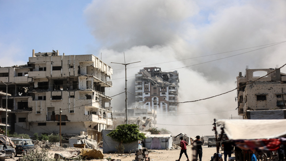 فلسطينيون يشاهدون انهيار برج مهنا وسط دخان كثيف، خلال غارة إسرائيلية على حي تل الهوا بمدينة غزة، 14 أيلول 2025. (أ ف ب)