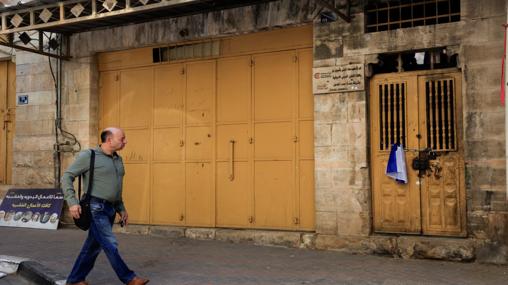 فلسطيني يسير بجوار علم إسرائيلي موضوع على باب منزل استولى عليه مستوطنون إسرائيليون في البلدة القديمة في الخليل بالضفة الغربية المحتلة. 3 أيلول 2025. (رويترز)