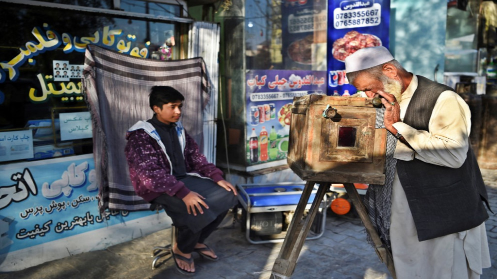 يلتقط المصور الأفغاني حاج ميرزامان (إلى اليمين) صورة لصبي بكاميرا صندوقية خشبية مصنوعة منزليًا تُعرف على رصيف في كابل، 13 تشرين الأول/ أكتوبر 2021. (أ ف ب)