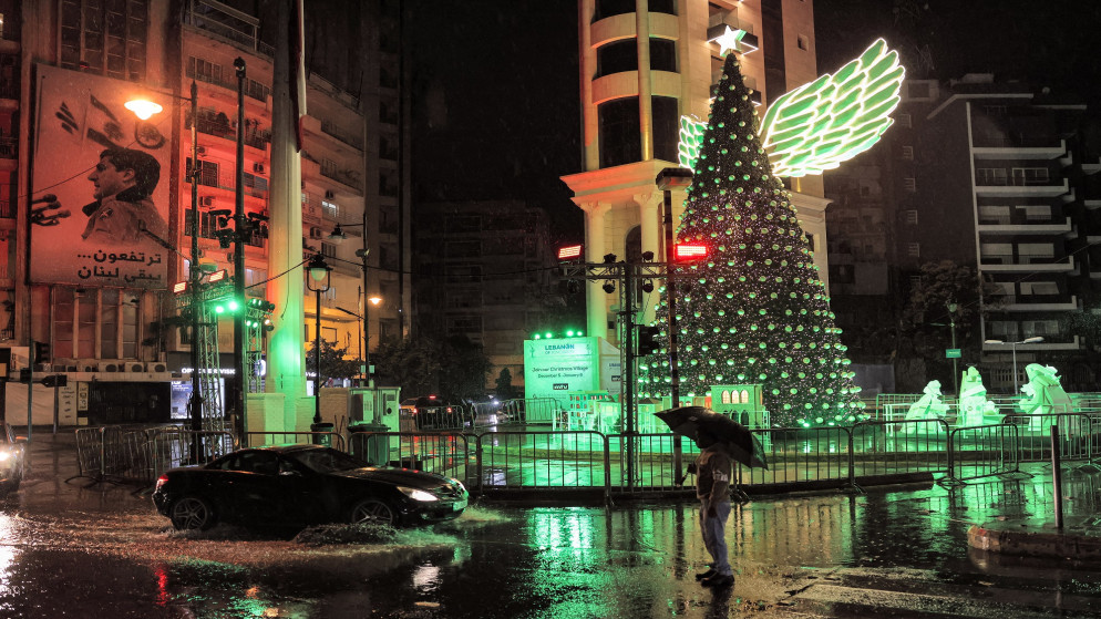 مرور سيارة في وقت متأخر من الليل مع هطول الأمطار أمام شجرة عيد الميلاد نصبت في الأشرفية الشرقية في العاصمة اللبنانية بيروت. 14/12/2021. (جوزيف عيد / أ ف ب)