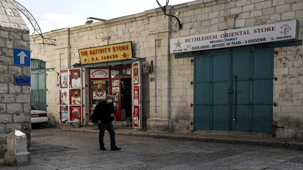 رجل يسير مرتديا الكمامة بجوار المحلات التجارية المغلقة في ساحة المهد الفارغة خارج كنيسة المهد في مدينة بيت لحم بالضفة الغربية المحتلة. 15 ديسمبر 2021. (أ ف ب)