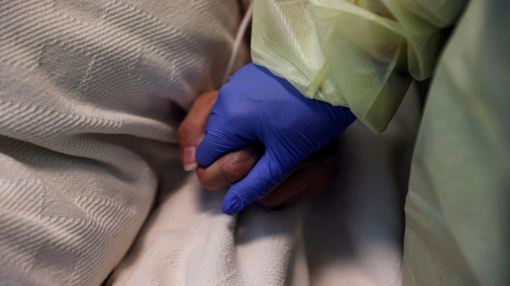 سيدة ترتدي معدات حماية شخصية تمسك بيد مريض مصاب بفيروس كورونا في غرفة عزل بمستشفى ماديسون في ريكسبورغ في الولايات المتحدة. 28 تشرين الأول/ أكتوبر 2021. (رويترز)